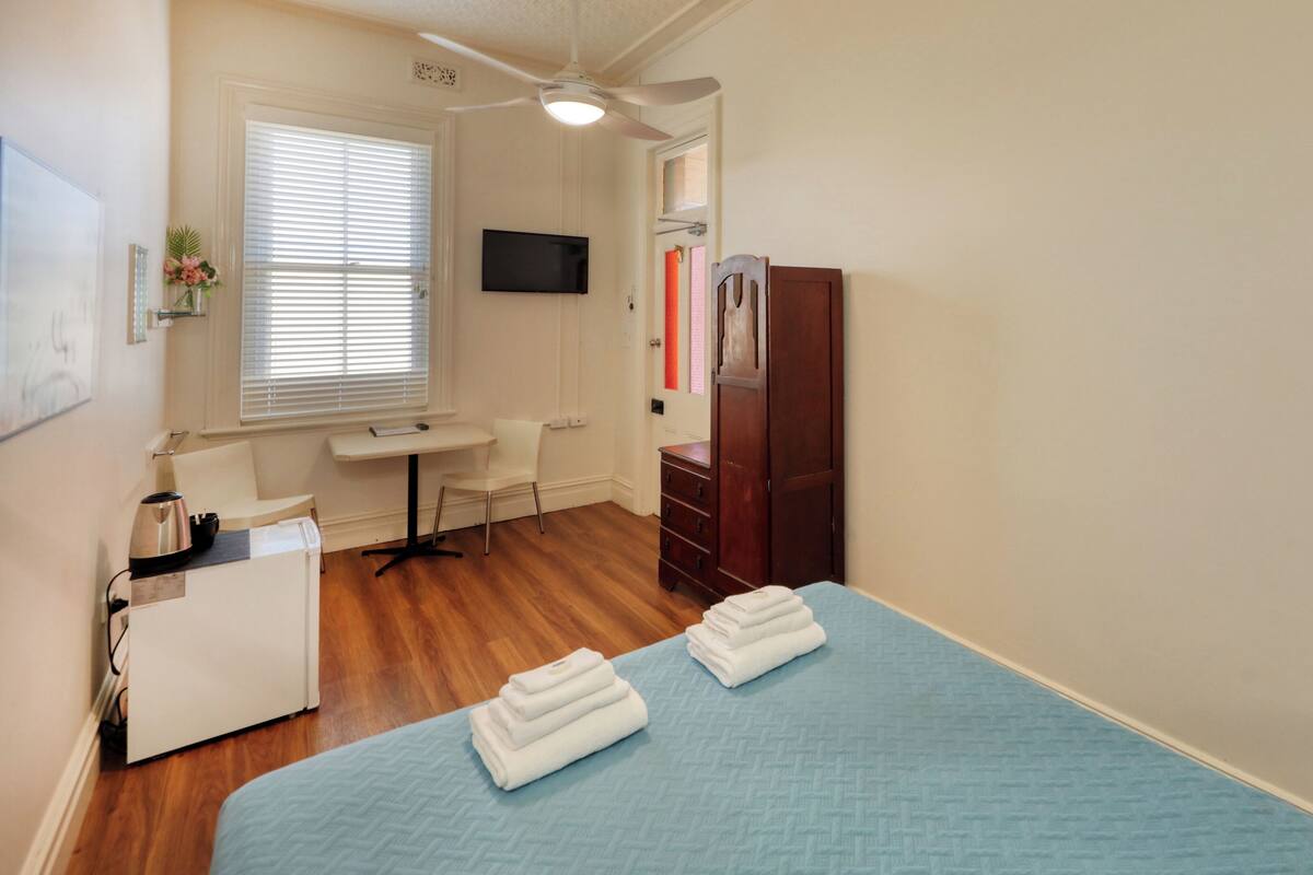 A bedroom with a bed, a desk, a chair, a wardrobe, and a television.