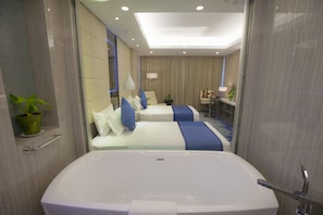 A modern hotel room with a large bathtub, two beds with blue and white bedding, a small desk, and a potted plant. - Grand Palace Hotel (Yangon)