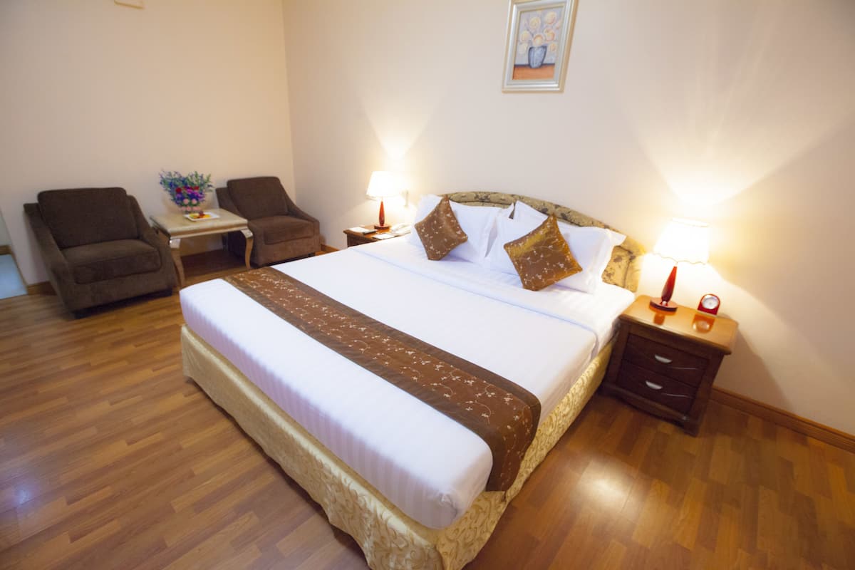 Una habitación de hotel con una cama grande, dos sillones, una mesita y dos lámparas de noche.