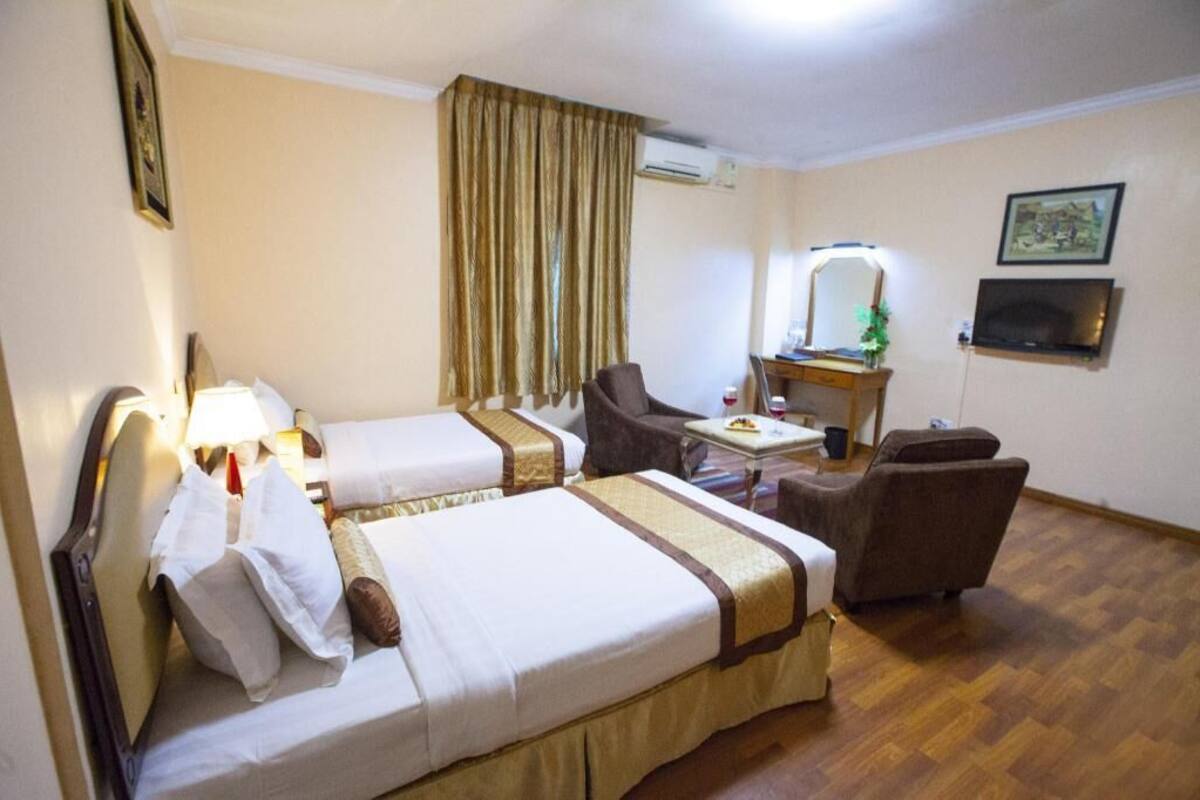 A hotel room with two beds, a desk with a chair, a television, and a mirror.