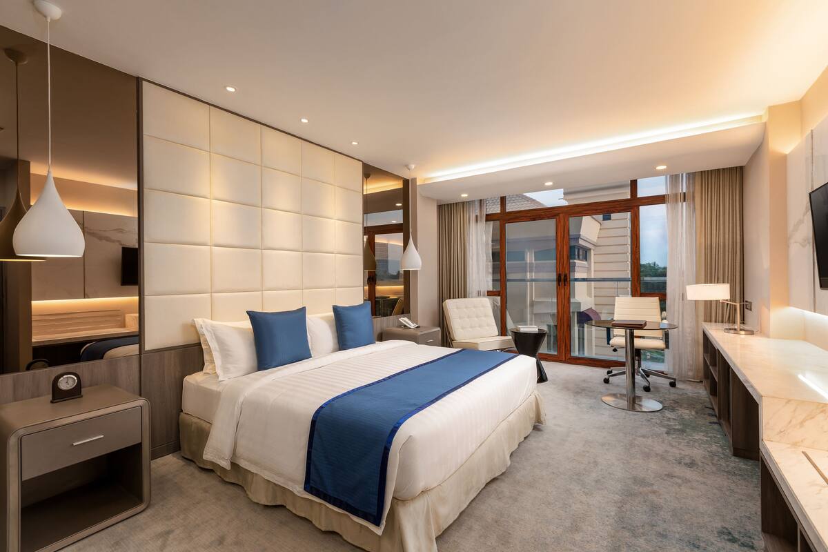 Habitación de hotel con una cama grande, un escritorio, una silla, un televisor y vistas a la ciudad.