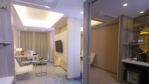 A modern hotel room with a sofa, a small table with a vase, a flat-screen TV mounted on the wall, and a minibar. - Grand Palace Hotel (Yangon)