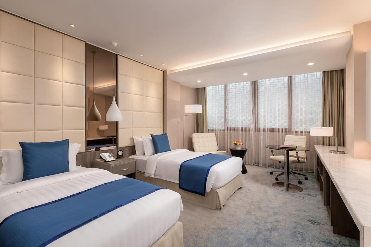 Habitación de hotel con dos camas, un escritorio, una silla, una lámpara, un teléfono y una ventana con cortinas.