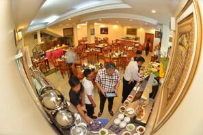A dining hall with multiple tables and chairs, a buffet setup, and a staircase in the background. - Grand Palace Hotel (Yangon)
