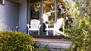 A porch with two white Adirondack chairs and a glass door leading to a garden. - Polperro Villas (Red Hill South)