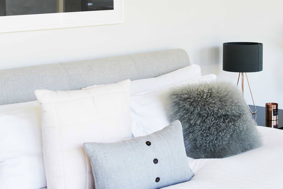 Un dormitorio con cama, almohadas, lámpara y un cuadro en la pared.