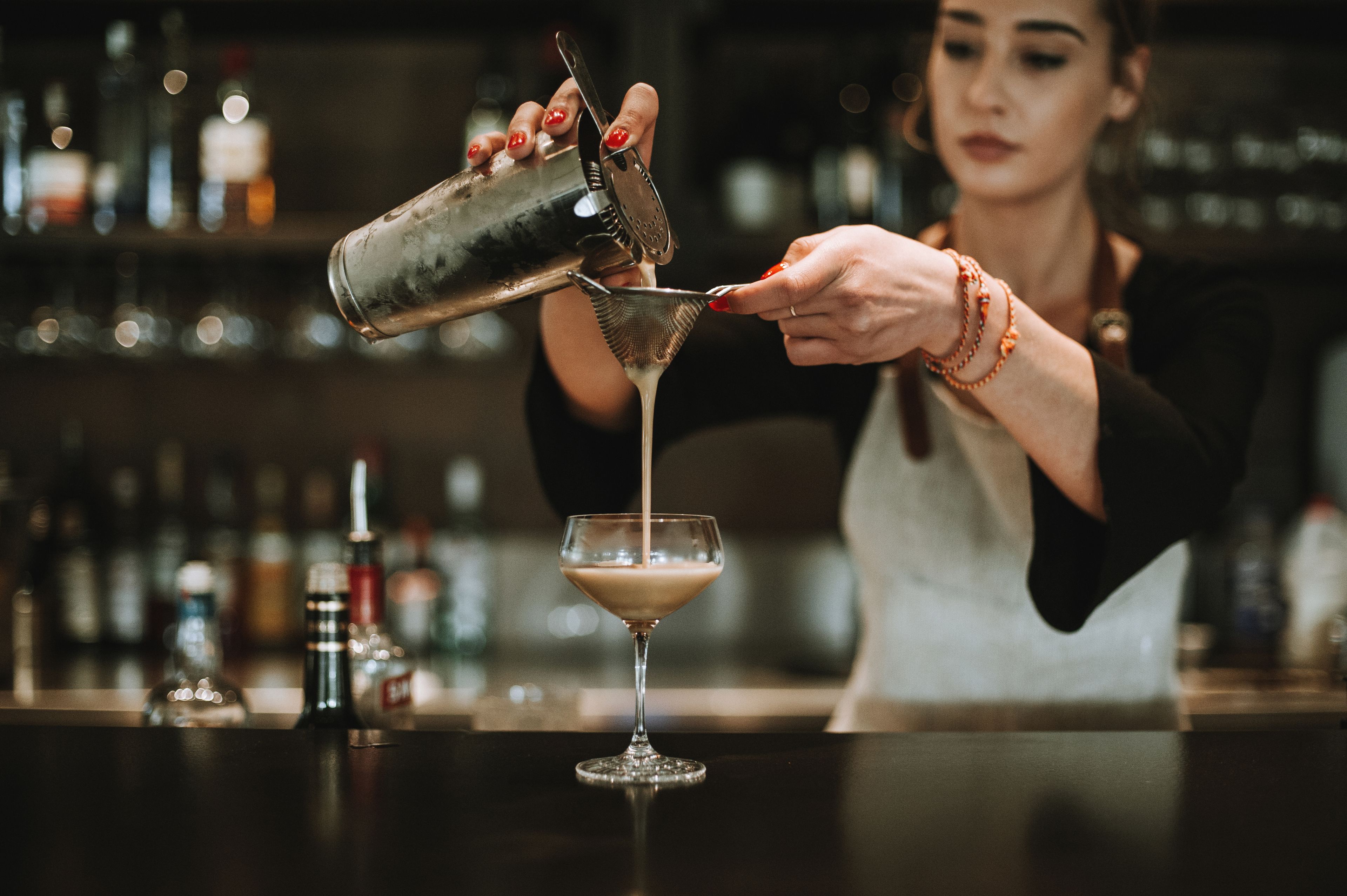 Un bartender sirviendo una bebida en una copa de martini.