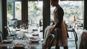 A restaurant with a table set for dining, a person in an apron, and a view of greenery outside. - Polperro Villas (Red Hill South)
