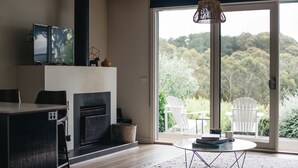 A modern living room with a fireplace, a dining area, and a large sliding glass door leading to a garden. - Polperro Villas (Red Hill South)
