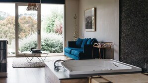 A modern living room with a large window, a blue sofa, a wooden coffee table, and a bathtub. - Polperro Villas (Red Hill South)