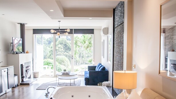 A modern hotel room with a large bed, a sitting area with a view, and a separate bathroom. - Polperro Villas (Red Hill South)
