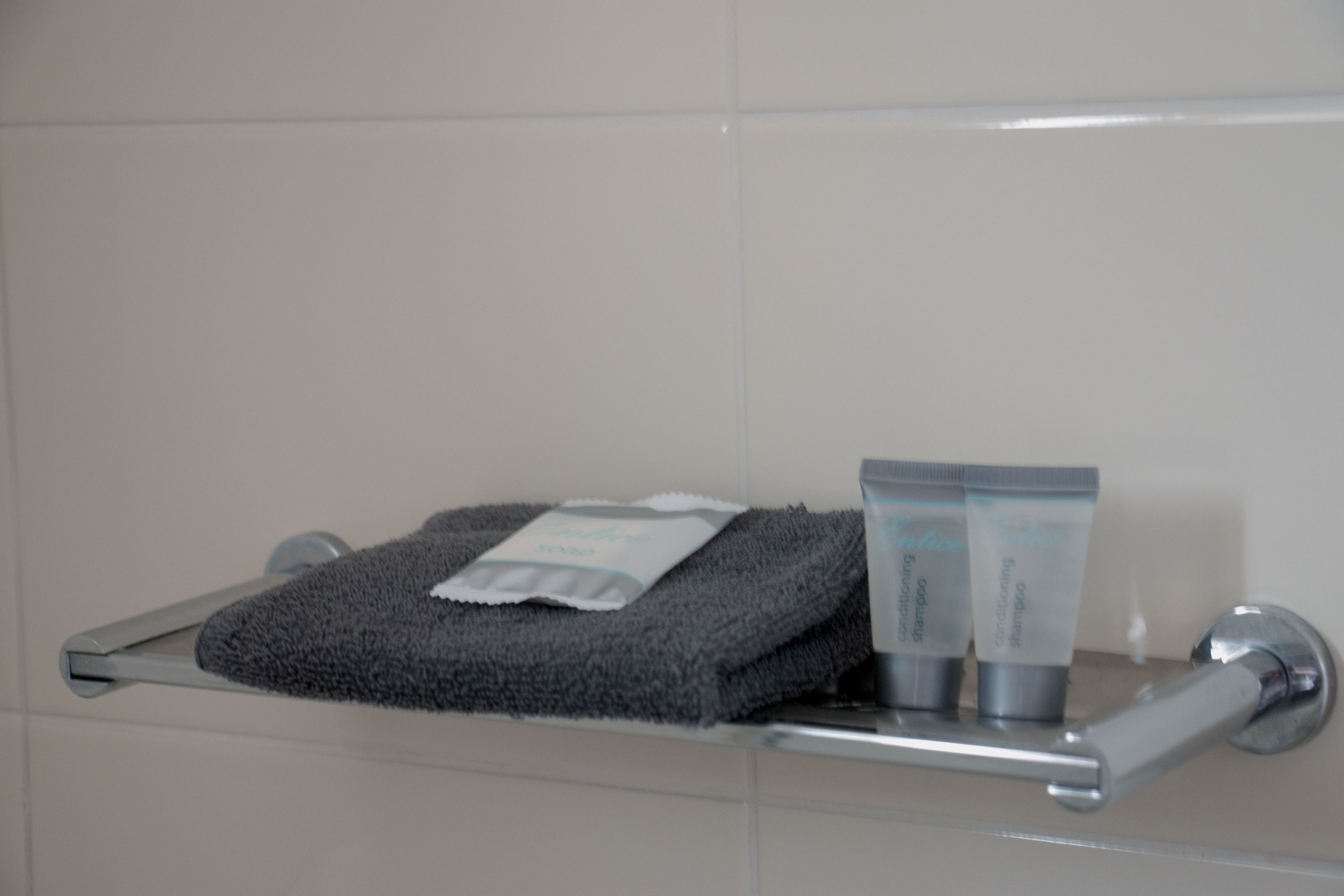 A bathroom with a towel rack holding a folded towel and two toiletry bottles.