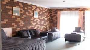 A hotel room with a brick-patterned wall, a large bed, a sofa, a small table, and a chair. - Highway Inn Motel (Hay)