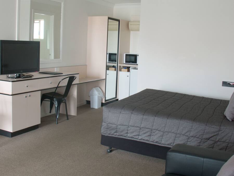 A hotel room with a bed, a desk, a chair, a television, a microwave, and a trash bin.