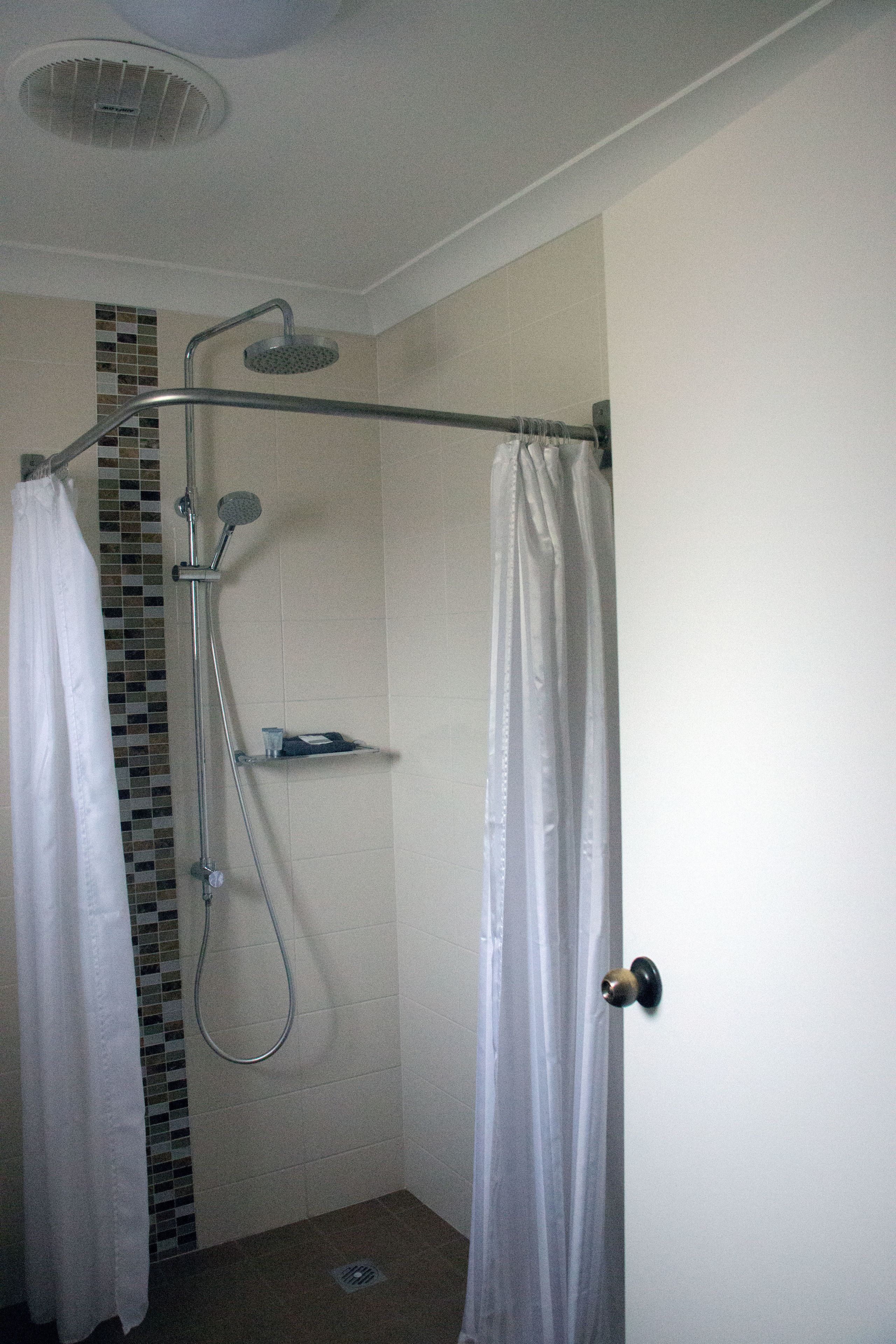 A shower area with a showerhead, a handheld shower, and a glass shelf.