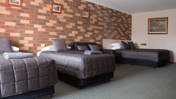 A hotel room with three beds, a brick-patterned wall, and framed pictures. - Highway Inn Motel (Hay)