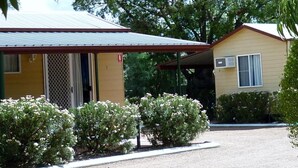 Un motel à deux étages, avec un toit rouge et un revêtement de couleur beige, entouré de verdure et doté d’une allée en gravier.