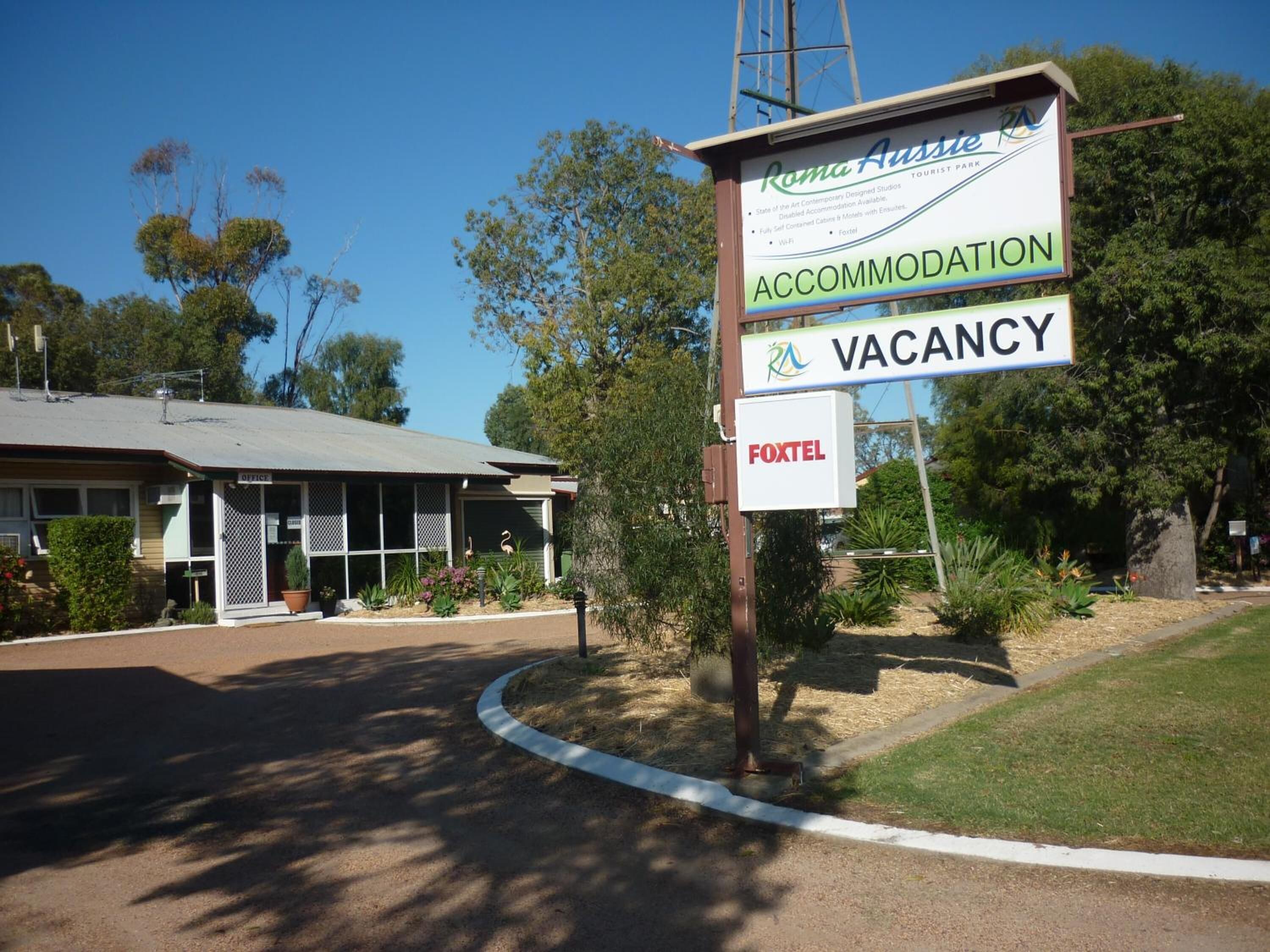 A signboard for a tourist park named "Roma Aussie" indicating accommodation and vacancy availability.
