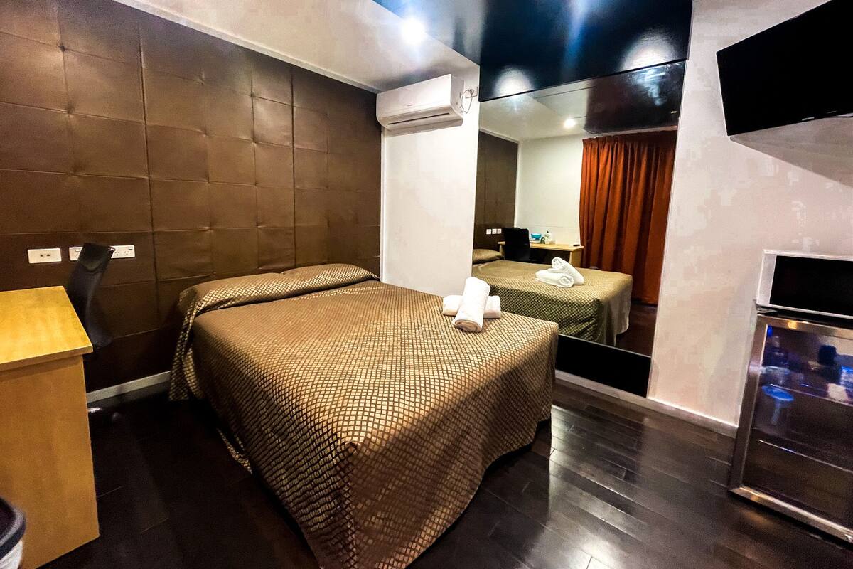 Una habitación de hotel con dos camas, un escritorio de madera, un espejo y televisión integrada.