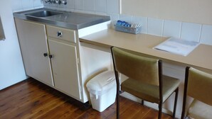 Une cuisine équipée d’un évier, de placards, d’un plan de travail, d’une chaise et d’une poubelle.