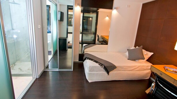 Une chambre d’hôtel moderne équipée d’un lit, d’un bureau, d’une chaise et d’une douche à parois de verre.