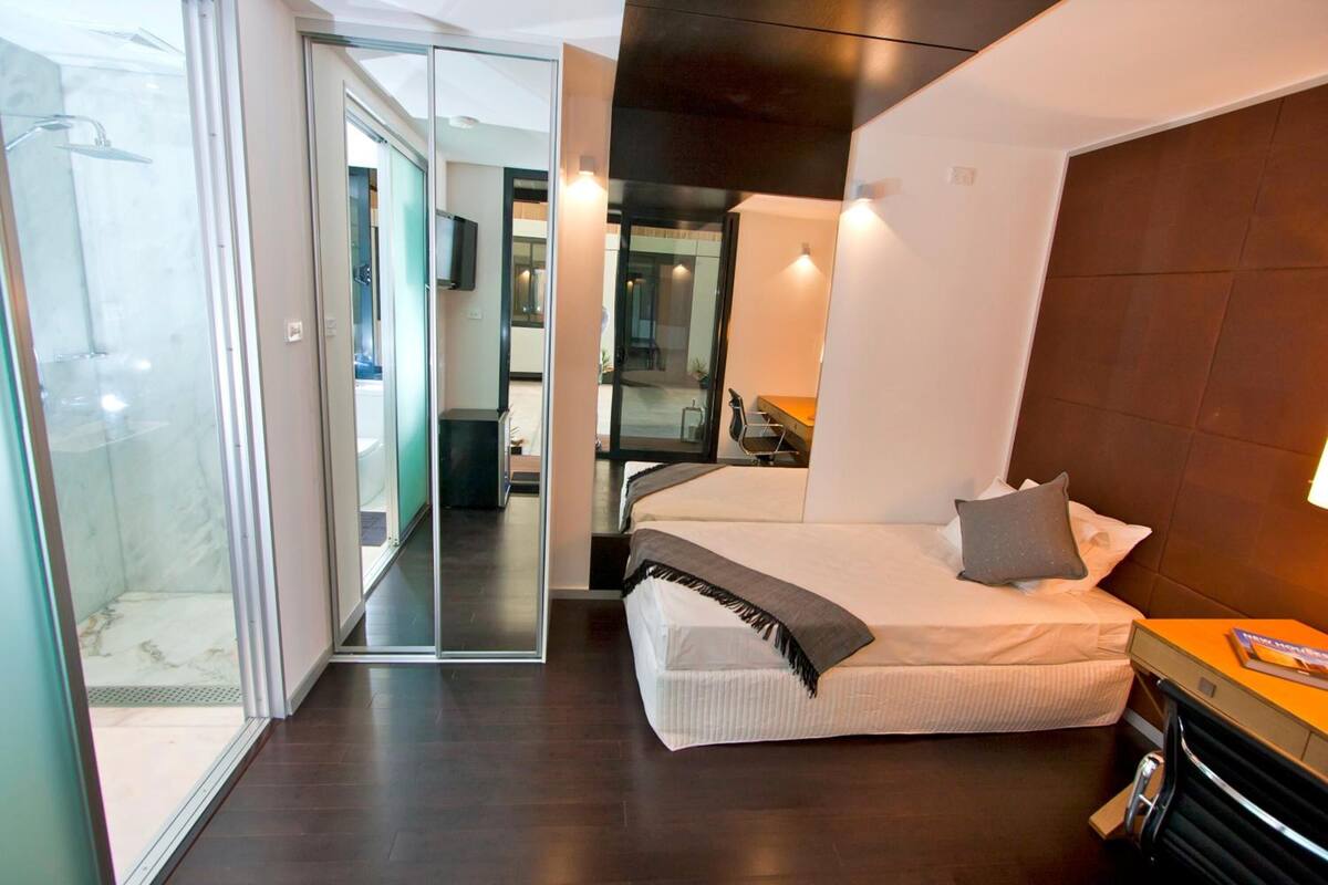 Una habitación de hotel moderna con cama, escritorio, silla y cabina de ducha de vidrio.