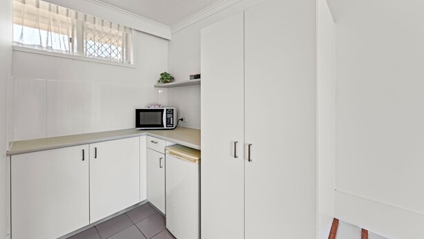 A compact kitchen with white cabinets, a microwave, and a small window with blinds. - Pottsville Beach Motel (Pottsville)