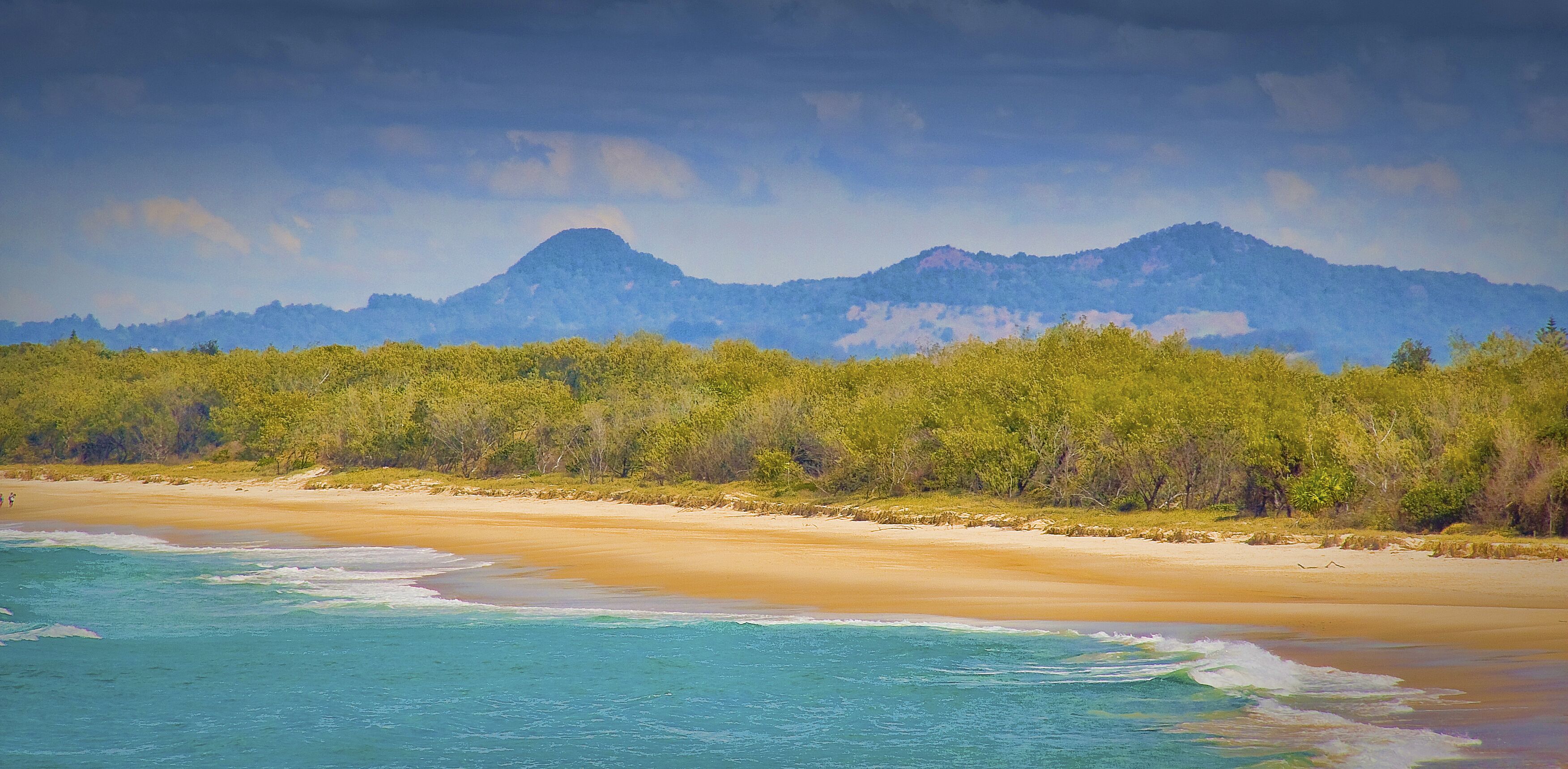 A beach with clear turquoise waters, a sandy shore, and a forested hill in the background.
