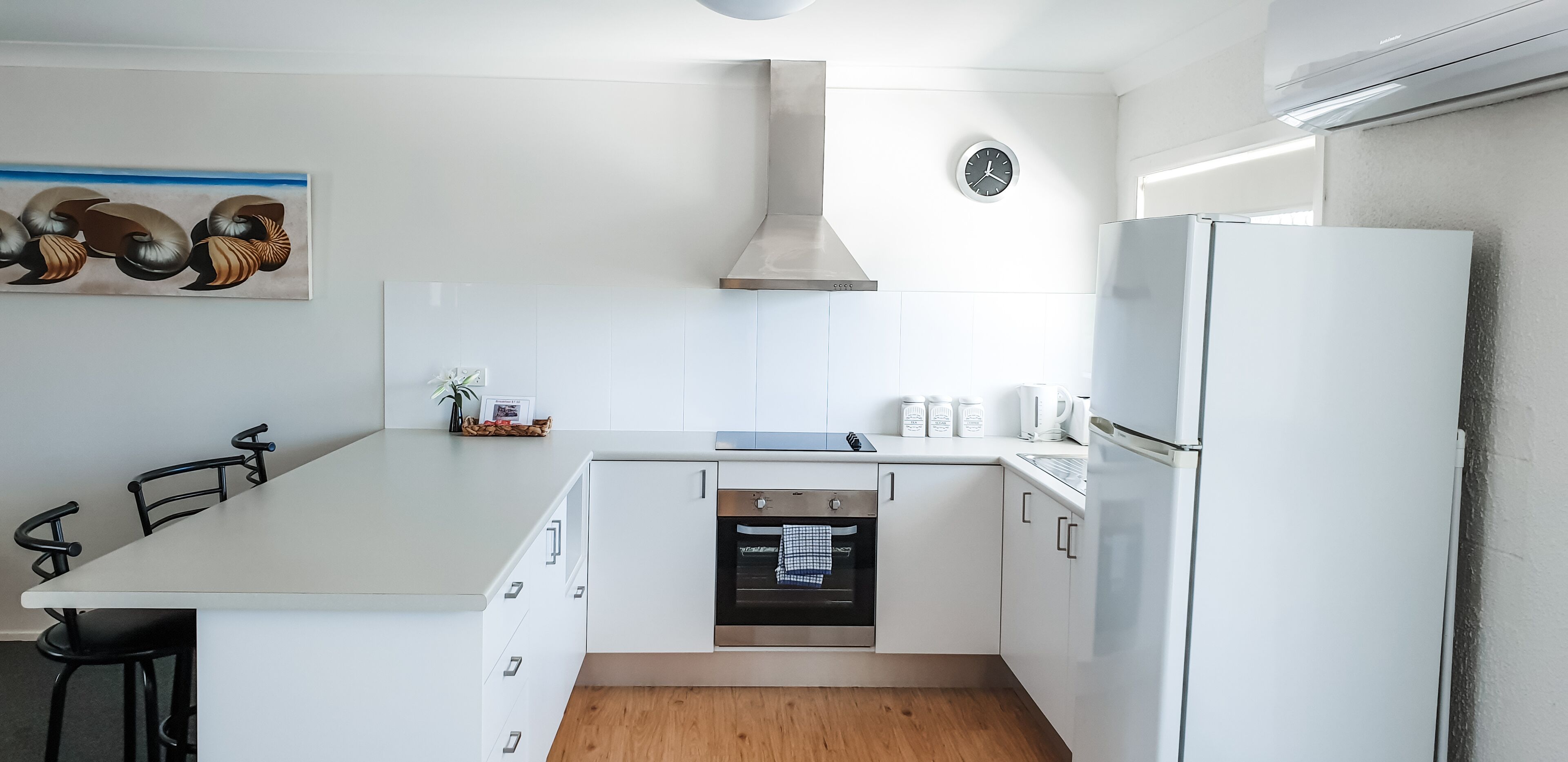 A modern kitchen with white cabinetry, a built-in oven, and a stainless steel range hood.