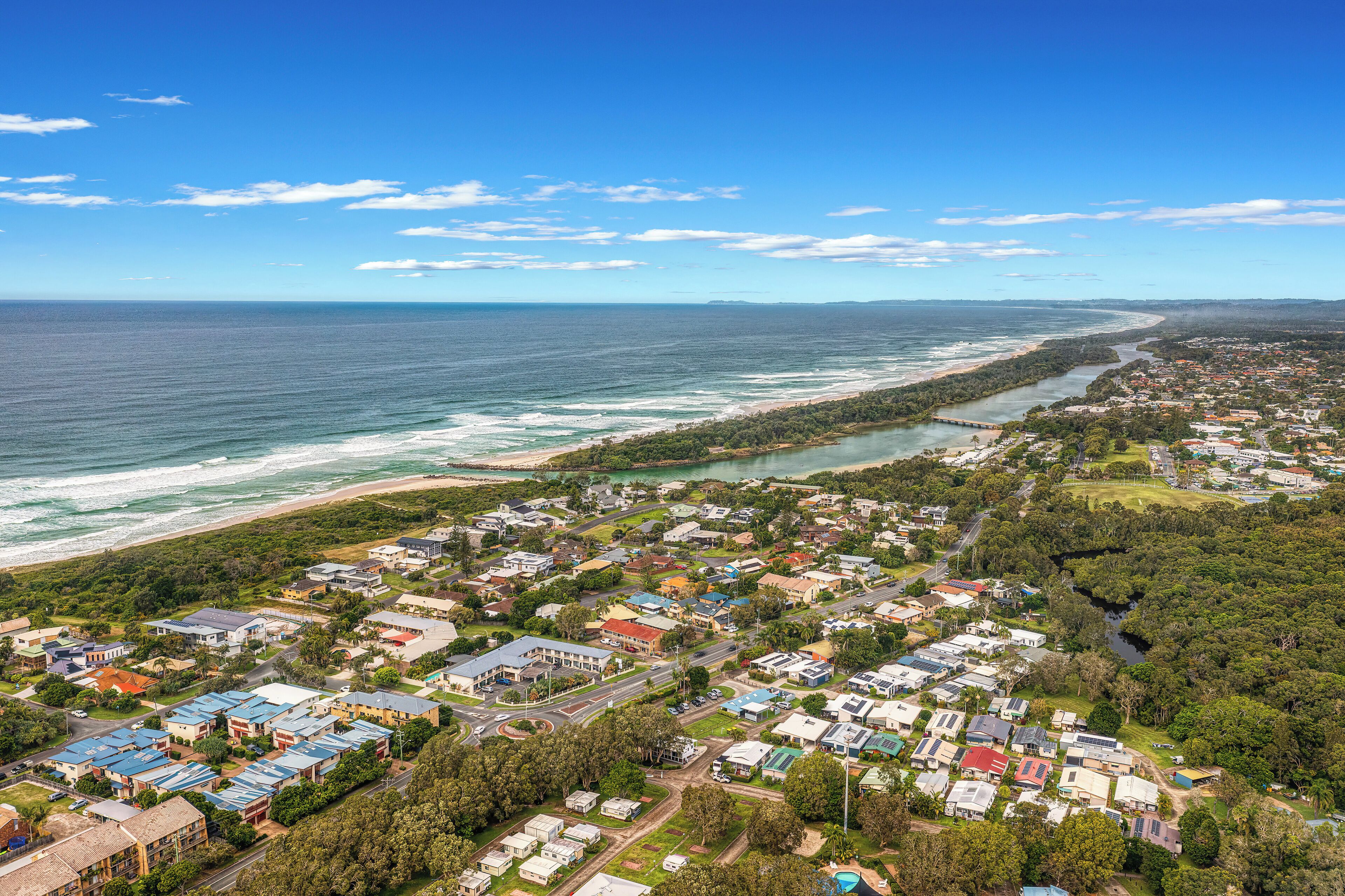 An aerial view of a coastal town with beachfront properties, a river running through the center, and a mix of residential and commercial buildings.