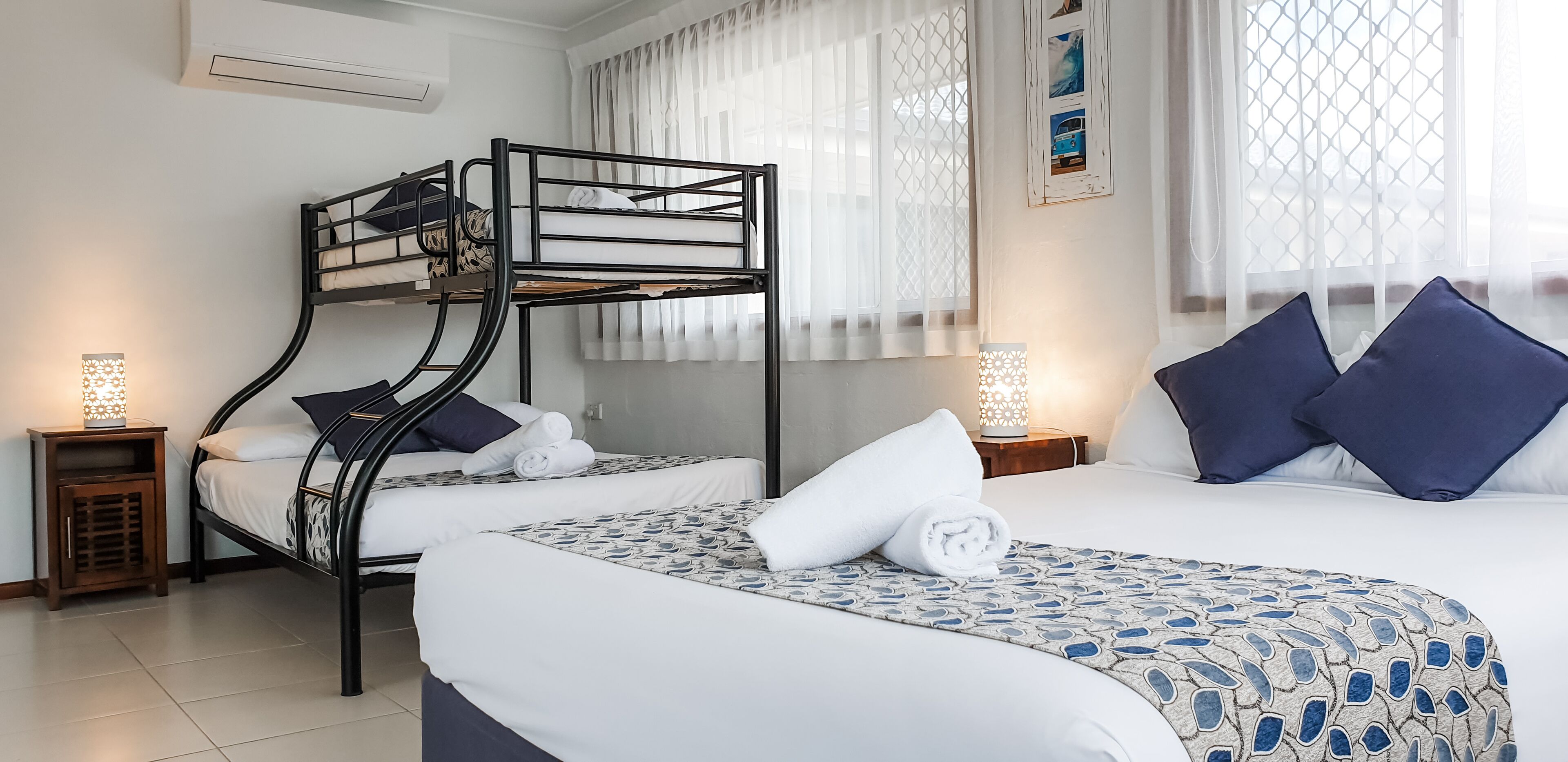 Une chambre avec un lit superposé, comportant deux lits, chacun avec un oreiller et une serviette enroulée. Il y a deux tables de chevet avec des lampes.