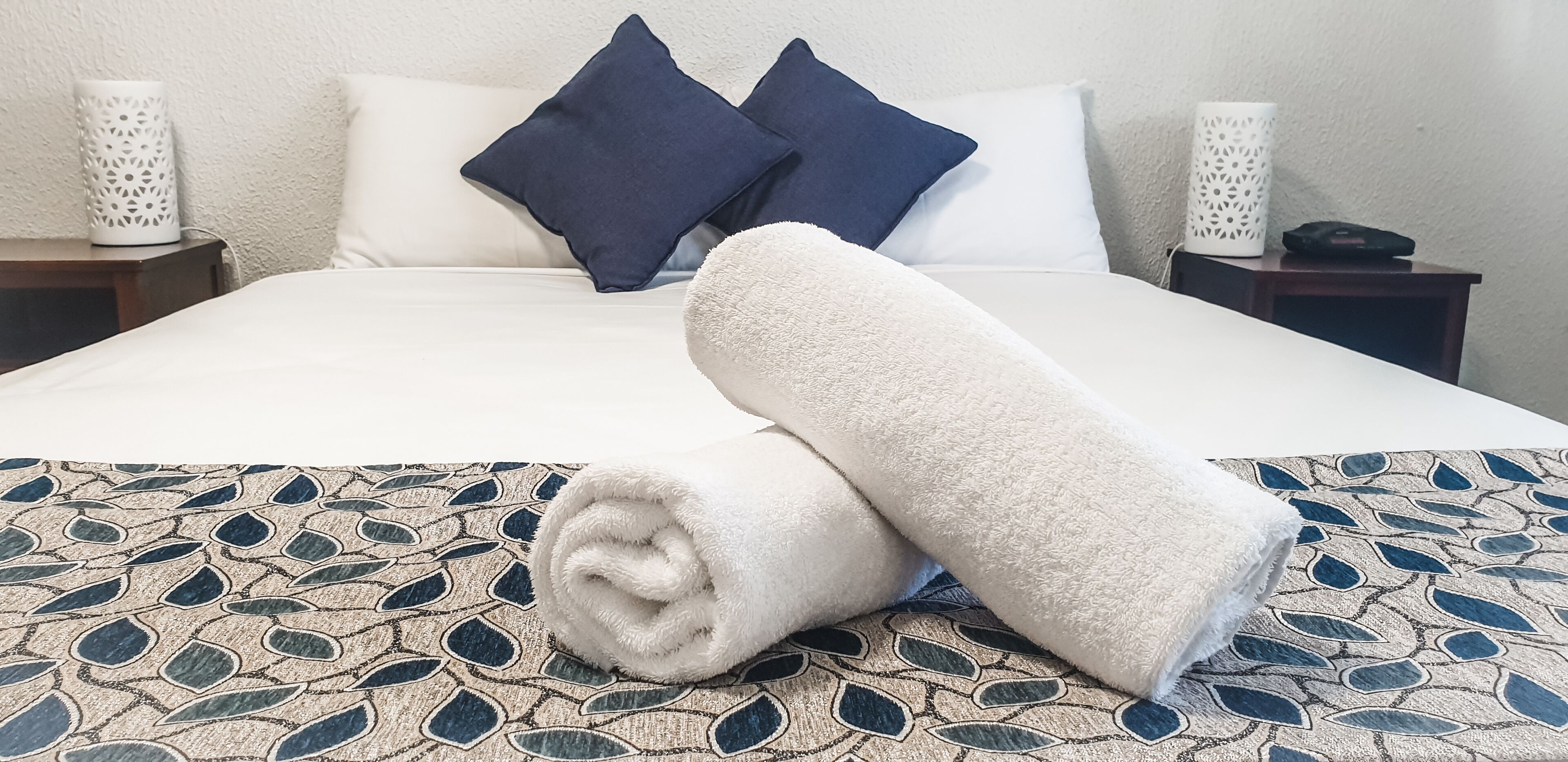 Un llit ben arropat amb un estovat estampat, dos coixins i una tovallola enrotllada en una habitació d'hotel.
