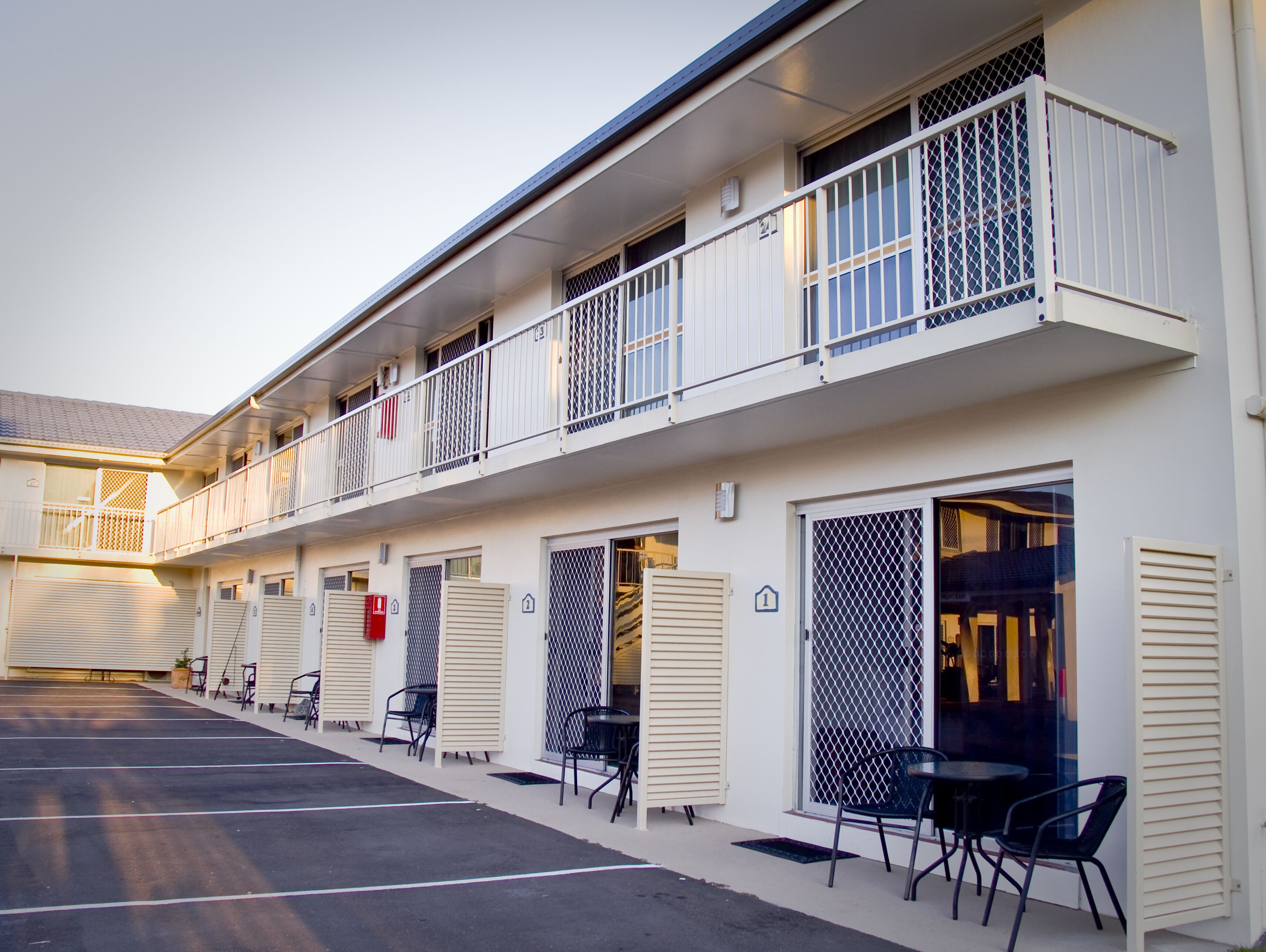 A two-story motel with individual rooms, outdoor seating, and a covered parking area.