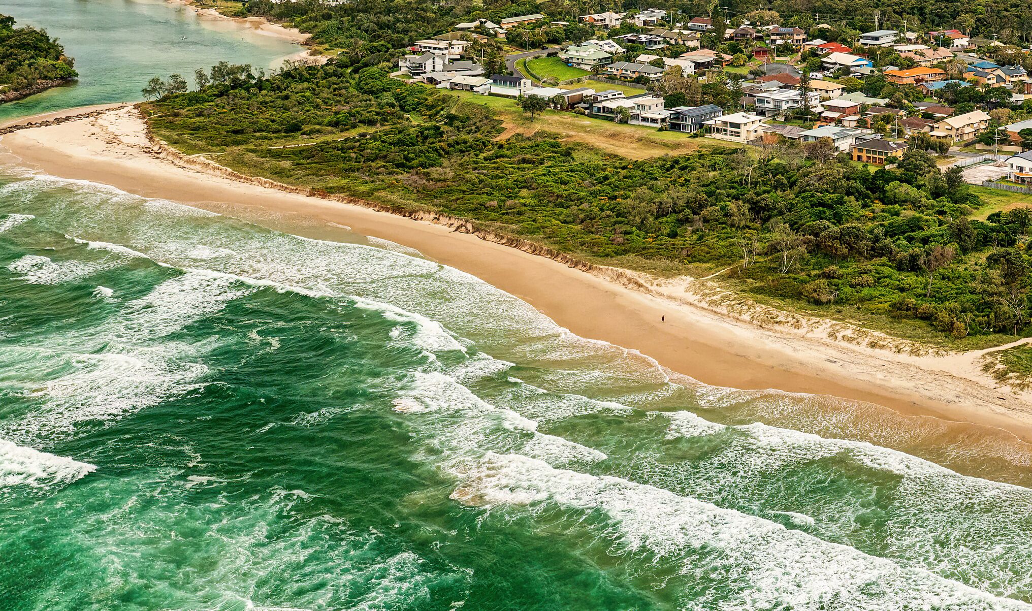 An aerial view of a coastal area with a sandy beach and a residential neighborhood.