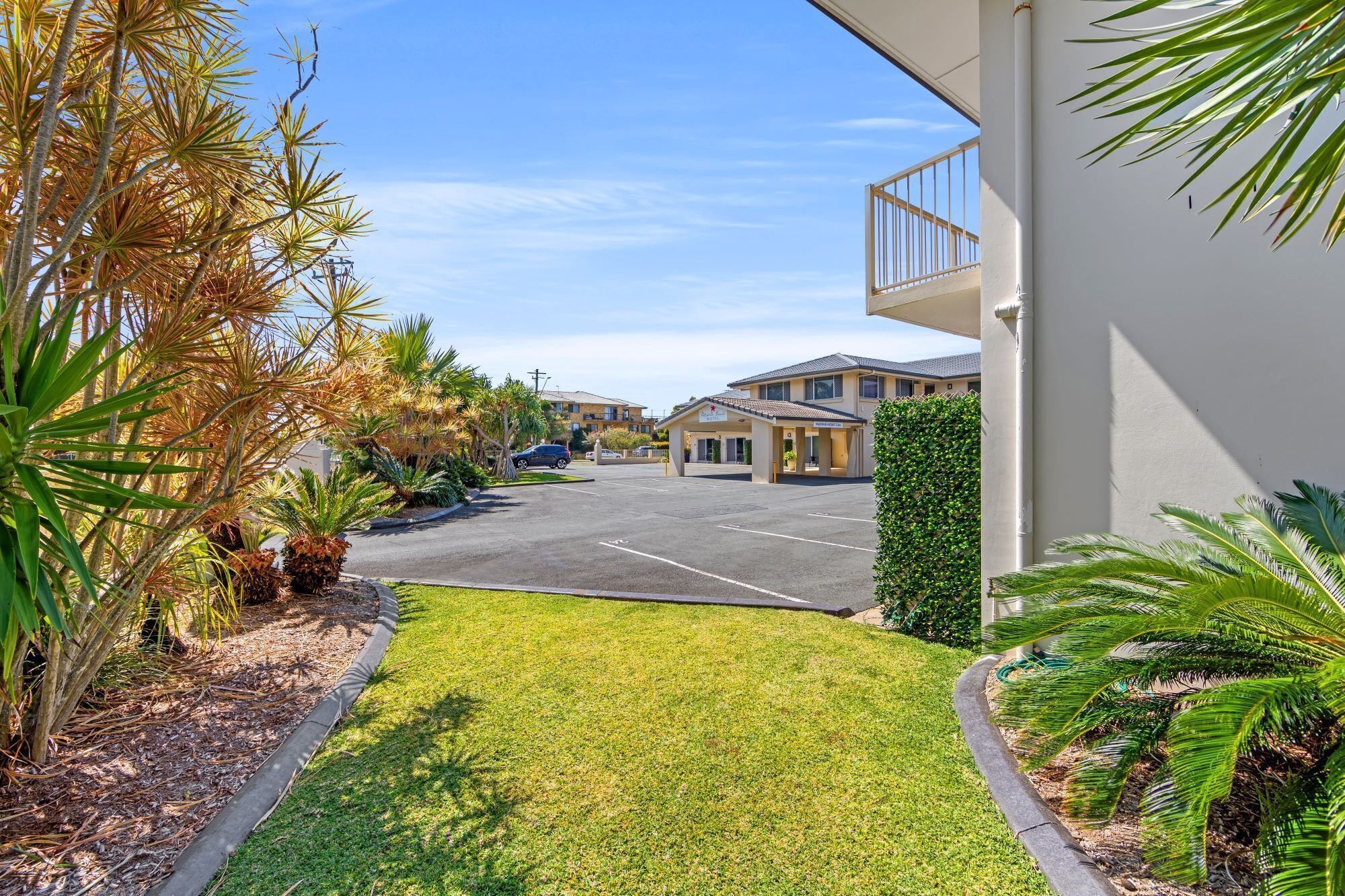 A hotel with a parking lot, a covered walkway, and a well-maintained lawn.