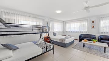 Een moderne hotelkamer met stapelbedden, een slaapbank, een bijzettafeltje en een plafondventilator.
