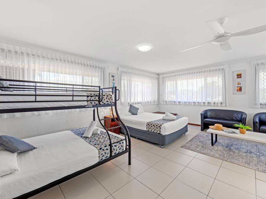 A modern hotel room with bunk beds, a sofa, a coffee table, and a ceiling fan.