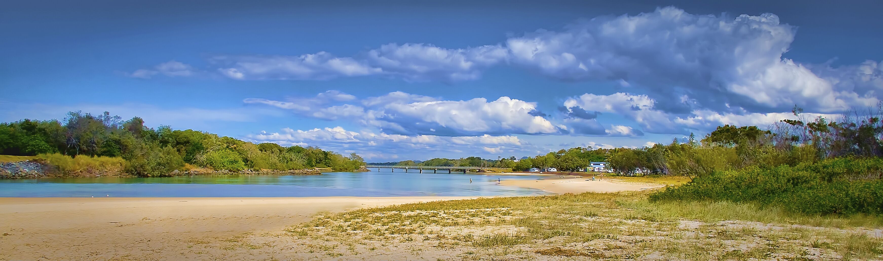 Une plage avec une rivière, un pont et de la verdure.
