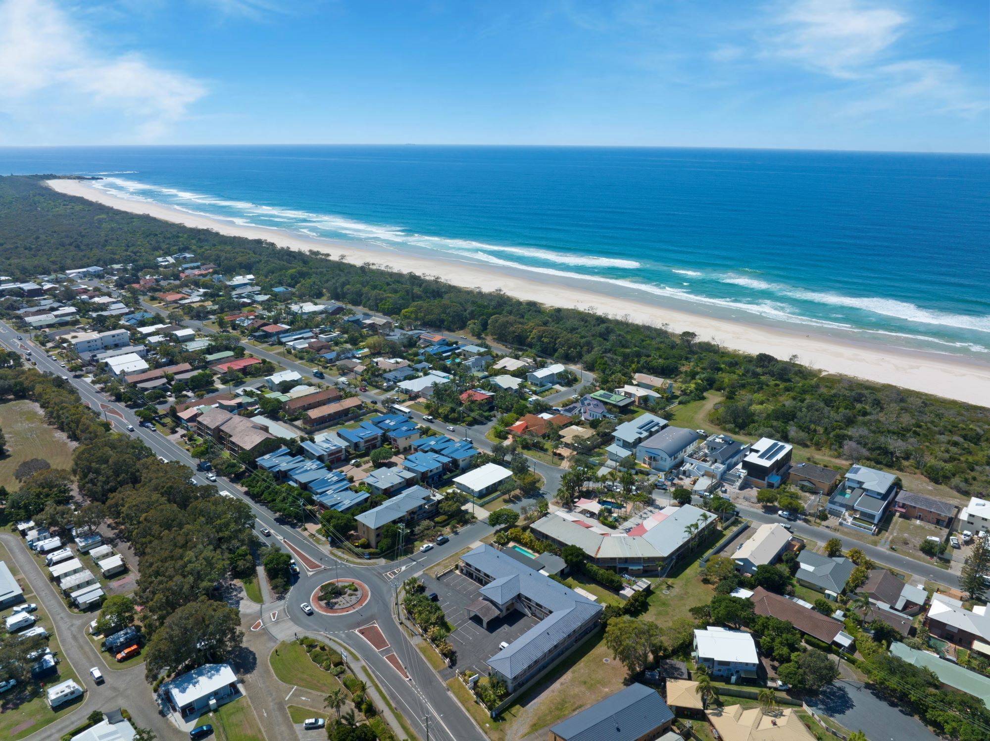 An aerial view of a coastal residential area with houses, roads, and a beach.
