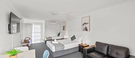 A modern hotel room with a bed, a desk, a chair, a sofa, and a TV.