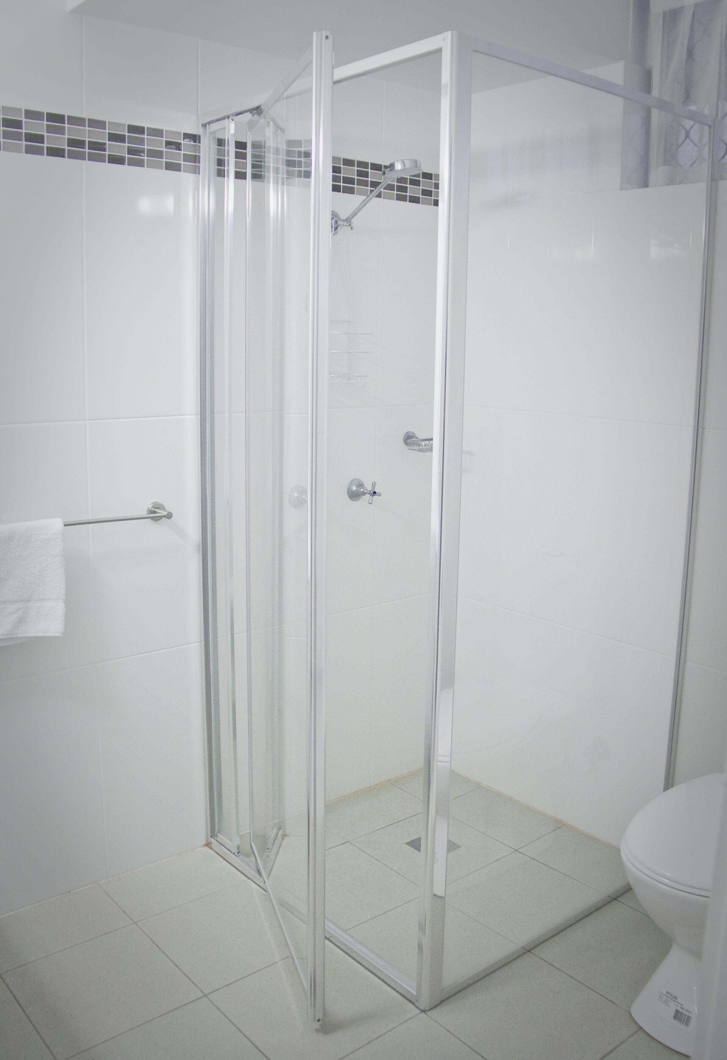 A modern bathroom with a glass-enclosed shower, white tiles, and a toilet.