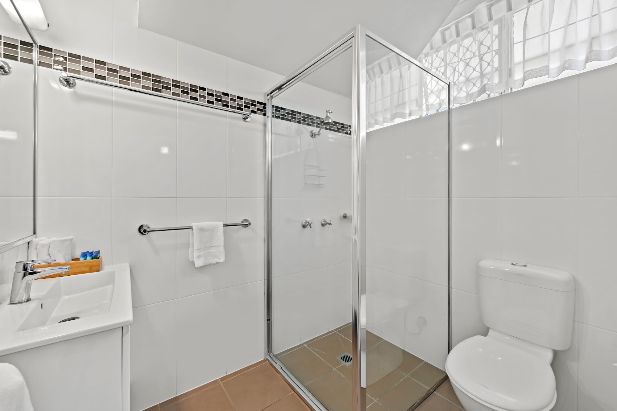 A modern bathroom with a glass-enclosed shower, a white toilet, and a sink with toiletries.
