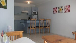 Un espacio habitable compacto con kitchenette, una zona de comedor con sillas de madera y un sofá.