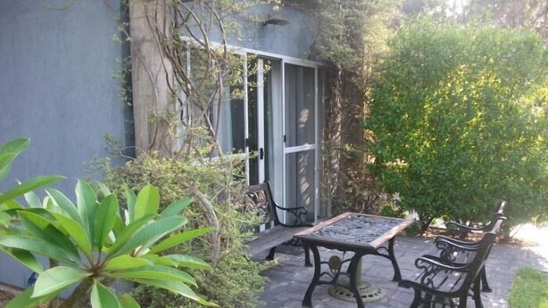 Un patio con mesa y sillas, rodeado de follaje y un edificio con puerta corrediza.