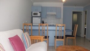 Un espacio habitable compacto con sofá, una pequeña mesa de comedor y una zona de kitchenette.