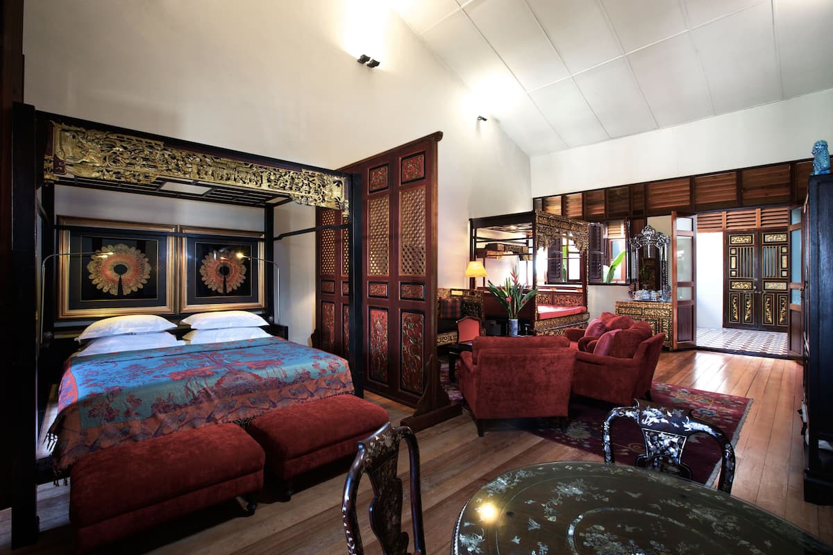 Une chambre à l’ancienne, dotée d’un grand lit, de fauteuils à revêtement rouge et d’une armoire en bois.