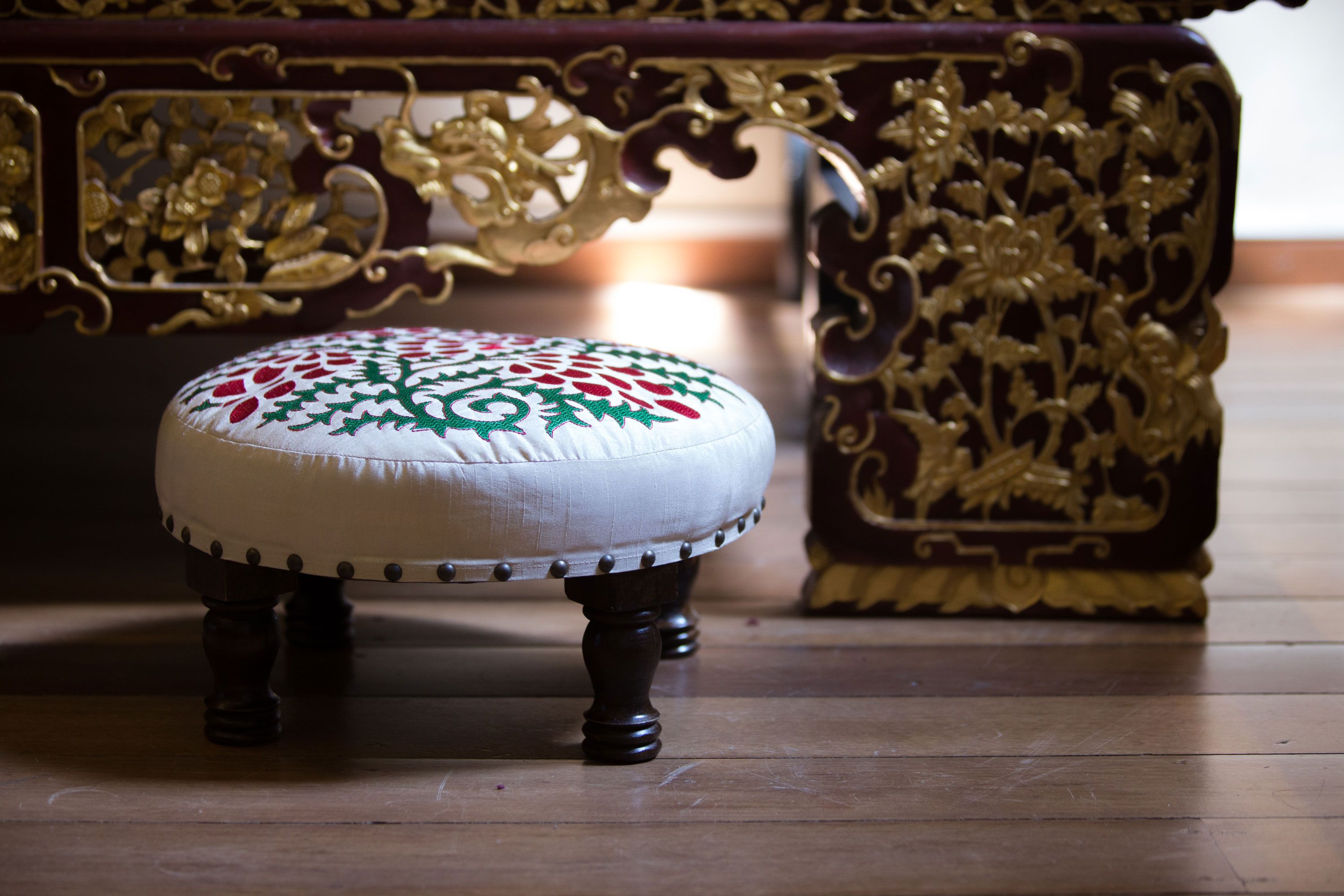 A round, upholstered stool with a floral pattern, placed on a wooden floor.