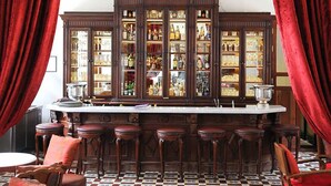 Un bar con suelo a cuadros, taburetes de madera y un amplio mueble lleno de botellas.