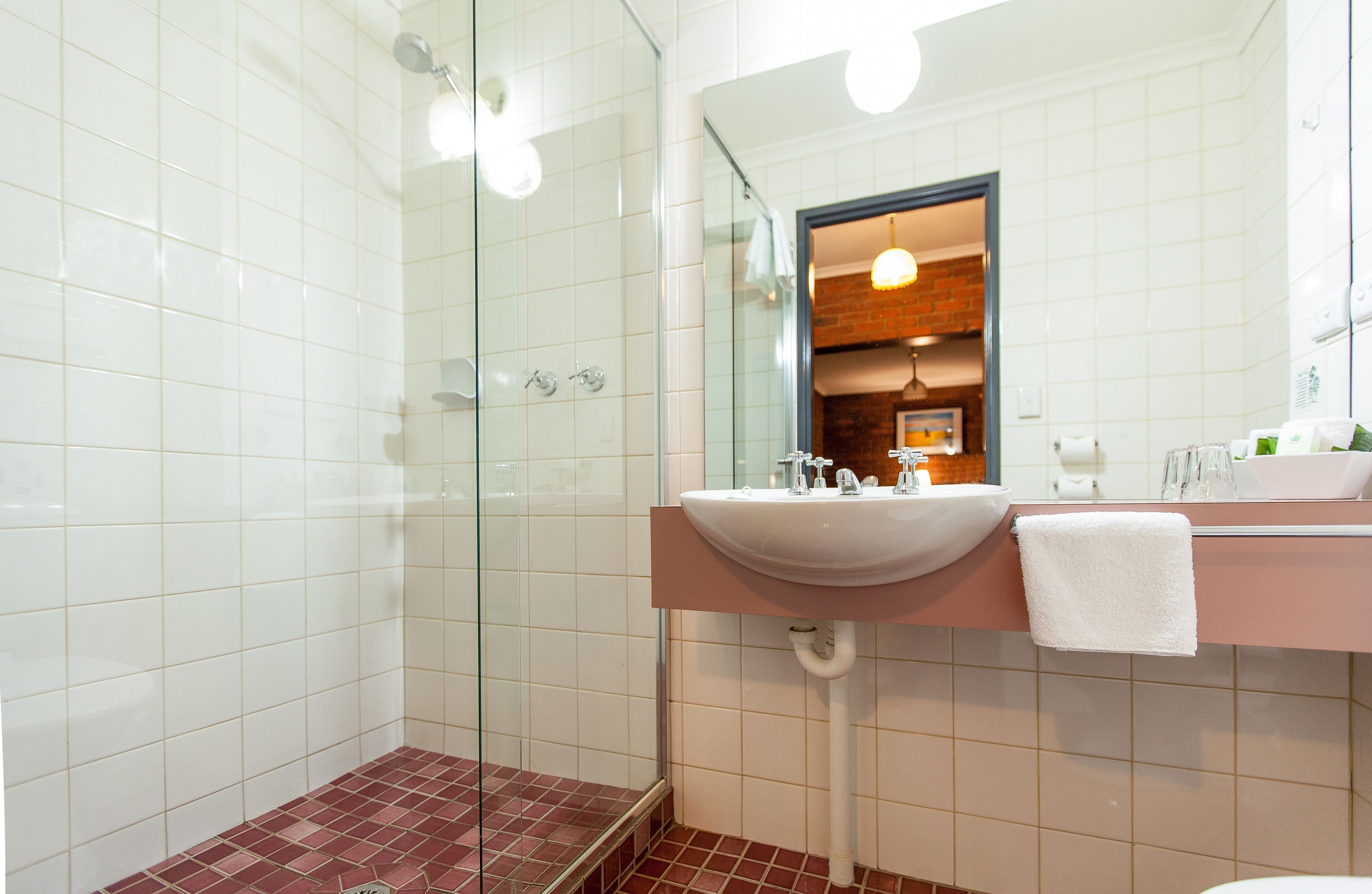 A bathroom with a glass shower enclosure, a sink with a mirror, and a towel hanging on the wall.