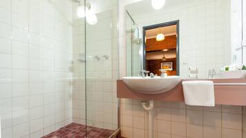 Een badkamer met een douchecabine van glas, een wastafel met spiegel en een handdoek aan de muur.